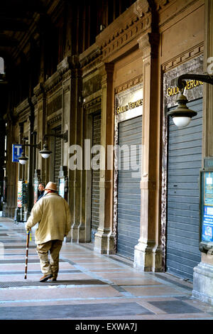 Un vieil homme en passant devant une rangée de boutiques fermées à Bologne, Italie Banque D'Images