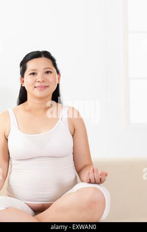 Femme enceinte assis avec les mains de genou et souriant, Banque D'Images