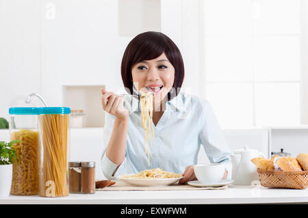 Young woman eating spaghetti et souriant à la caméra, Banque D'Images