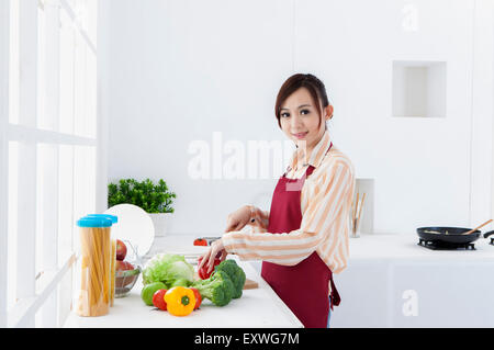 Young woman cutting vegetables et souriant à la caméra, Banque D'Images