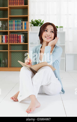 Jeune femme assise sur le sol et l'écriture avec sourire, Banque D'Images