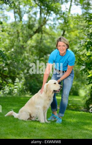 Femme mature avec un golden retriever dans jardin Banque D'Images