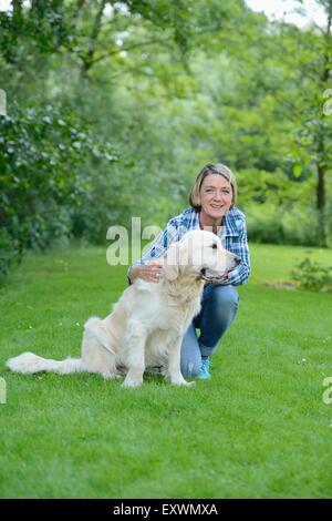 Femme mature avec un golden retriever dans jardin Banque D'Images