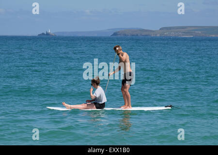 St Ives, Cornwall, UK : Jeune homme et femmes partagent un paddle-board, sur l'eau à St Ives. Banque D'Images