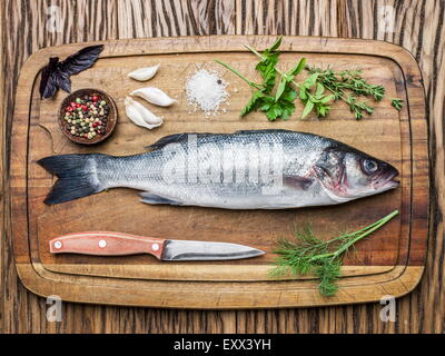 Poisson - sea bass sur une planche en bois avec des épices et fines herbes. Banque D'Images