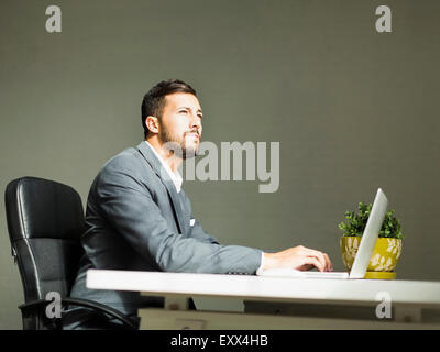 Jeune homme assis à un bureau et à l'aide d'ordinateur portable Banque D'Images
