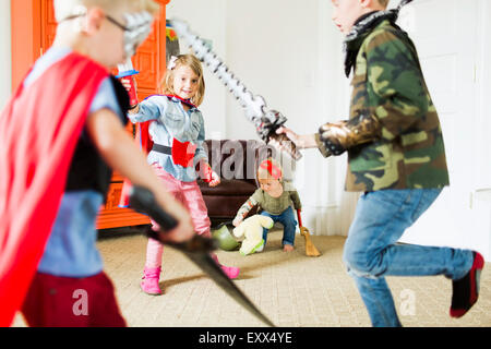 Enfants (2-3, 4-5, 6-7) wearing superhero costumes jouant à la maison Banque D'Images