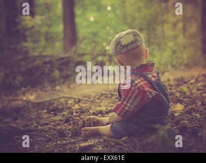 Enfant assis dans la forêt à la fin de l'été. Garçon photographié par derrière Banque D'Images