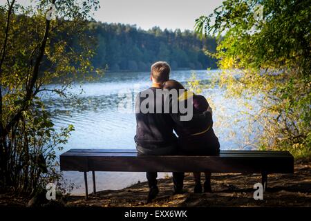 Silhouettes d'hugging couple sitting on bench contre le lac au coucher du soleil. Vintage photo. Banque D'Images