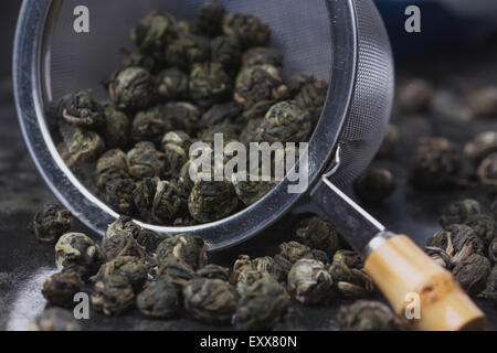 Perles de thé vert dans la crépine métallique vintage sur le plateau de métal noir Banque D'Images