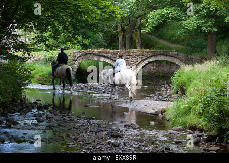 Deux cavaliers crossing Wycoller Beck, Breistroff-la-Grande, Lancashire Banque D'Images