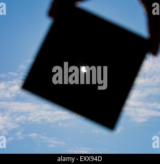 Éclipse partielle du soleil. Homme couvrant un fort ensoleillement par plaque sombre et montre sun eclipse. man main silhouette sur ciel bleu. Banque D'Images