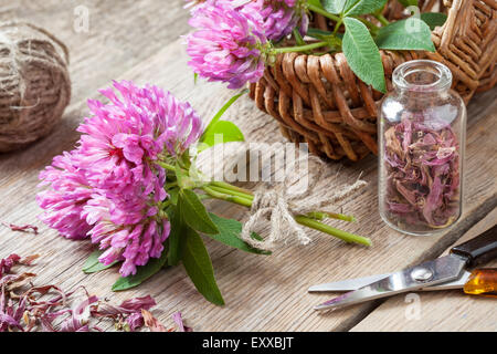 Bouquet de trèfle, de bouteille avec de l'herbe séchée et panier de fleurs sur table en bois. Banque D'Images