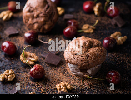 Muffins au chocolat sur fond sombre, poudre de cacao, noix, morceaux de chocolat et cerises comme décoration, selective focus Banque D'Images