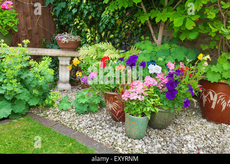 Coin ombragé d'un jardin avec les conteneurs remplis de fleurs colorées Banque D'Images