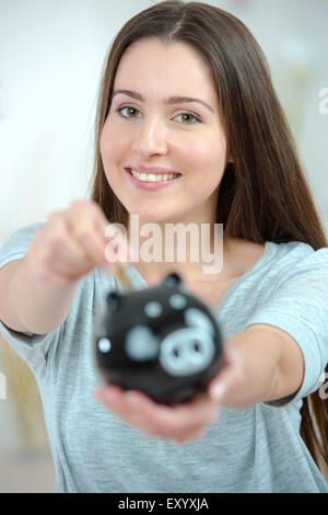 Woman putting coins into a piggy bank Banque D'Images
