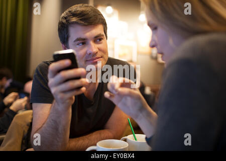 L'homme à l'aide de téléphone mobile pendant une réunion avec girl in cafe Banque D'Images