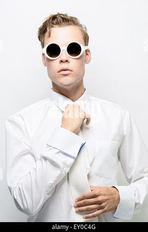Un jeune homme, modèle masculin, adjusting necktie, portant un costume tout blanc et lunettes de soleil. Un concept futuriste, concept de haute couture Banque D'Images