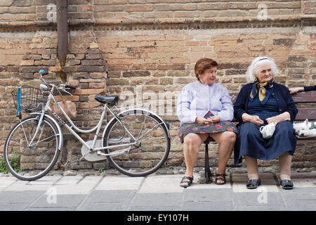 Deux dames âgées assis sur un banc de la rue à côté d'une location en face d'un mur de briques. Banque D'Images