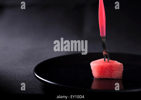 L'une des tranches de melon sur une plaque avec un tablier rose sur fond noir Banque D'Images