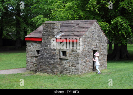 Fille regarde à l'intérieur de petit chalet en terre de conte de fées, Margam Country Park, Port Talbot, Pays de Galles du Sud. UK Banque D'Images