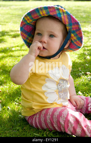 Portrait d'une petite fille assise sur l'herbe portant un chapeau de soleil Banque D'Images