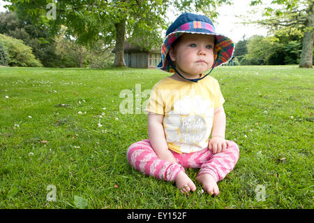 Petite fille assise sur l'herbe portant un chapeau de soleil à réfléchi Banque D'Images