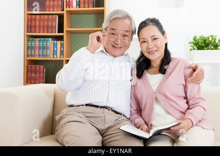 Senior couple sitting on sofa et souriant à l'ensemble, l'appareil photo Banque D'Images