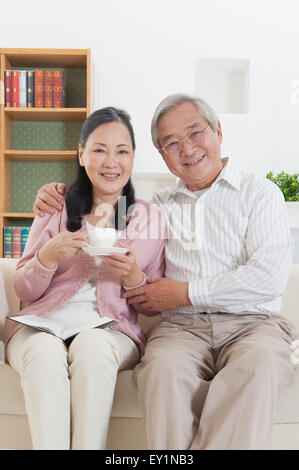 Senior couple sitting on sofa et souriant joyeusement à l'appareil photo, Banque D'Images