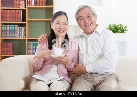 Senior couple sitting on sofa et souriant joyeusement à l'appareil photo, Banque D'Images