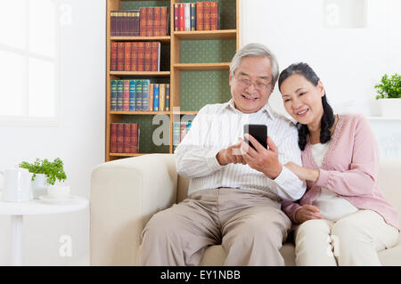 Couple assis sur le canapé à la recherche et le téléphone mobile avec sourire, Banque D'Images