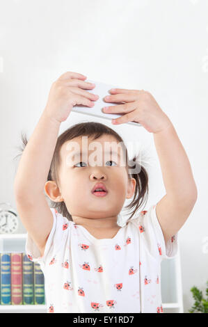 Little girl holding mobile phone and looking up, Banque D'Images