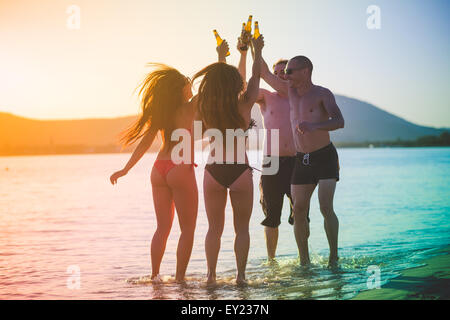Groupe de jeunes amis multiethnique les femmes et les hommes à la plage en été, le grillage et la consommation de bière de saut et de la danse - l'amitié, l'insouciance concept - filtre coloré Banque D'Images