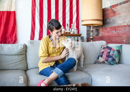 Young woman petting dog on sofa du salon Banque D'Images