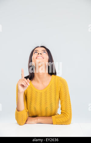 Jeune femme assise à la table et montre de l'index jusqu'à copyspace isolé sur fond blanc Banque D'Images
