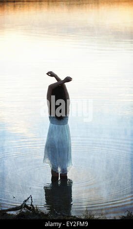 Une femme en robe blanche en eau peu profonde au crépuscule Banque D'Images