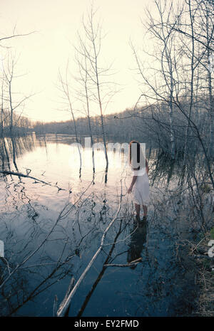 Une femme en robe blanche debout dans l'eau peu profonde à la tombée de la rive du lac de bya. Banque D'Images