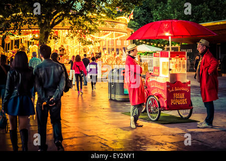 Un panier frais vente popcorn avec deux vendeurs se tenait en face d'un carrousel de foire traditionnelle Banque D'Images