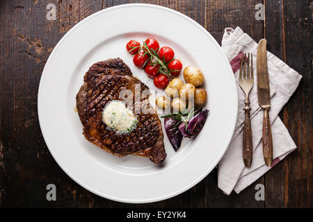 Ribeye Steak grillé au beurre d'herbes et pommes de terre bébé sur plaque blanche sur fond de bois Banque D'Images