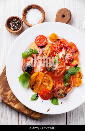 Frais salade de tomates mûres colorés avec de l'huile d'olive et vinaigre balsamique blanc sur fond de bois Banque D'Images