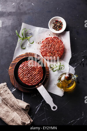 La viande de boeuf haché cru Burger steak escalopes et les assaisonnements sur fond de marbre noir Banque D'Images