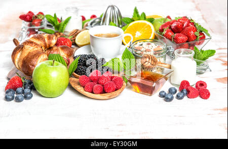 Le petit-déjeuner avec café, croissants, céréales, miel, céréales, baies fraîches, fruits orange, pomme, lait. Banque D'Images