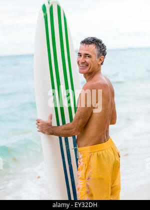Portrait of a senior male oceanside permanent tenant une planche de surf Banque D'Images