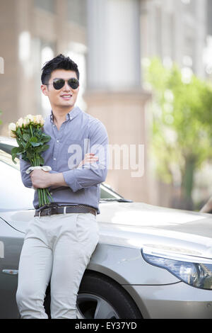 Jeune homme appuyé contre sa voiture avec un bouquet de fleurs Banque D'Images