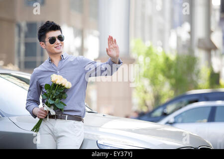 Jeune homme appuyé contre sa voiture avec un bouquet de fleurs Banque D'Images