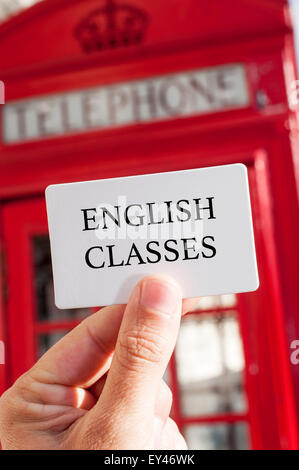 La main d'un homme avec une pancarte portant le texte anglais cours écrit en C, avec une cabine téléphonique rouge typique dans le bac Banque D'Images