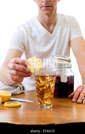 Man Putting tranche de citron sur le grand verre de thé glacé Banque D'Images
