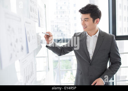 Young businessman writing on whiteboard in office Banque D'Images