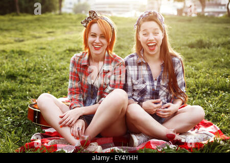 Deux jeunes femmes en riant Hipster Style Pin Up s'amusant à un pique-nique dans le parc au coucher du soleil Banque D'Images