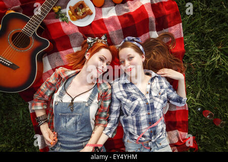 Young Beautiful Smiling Girls habillées de style pin up allongé sur un Plaid rouge sur l'herbe verte en été Parc. Vue d'en haut. Banque D'Images